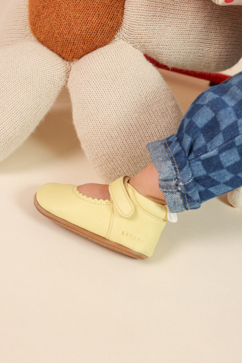 Bébé enfilant ses chaussons en cuir souple Lazare pieds nus en été
