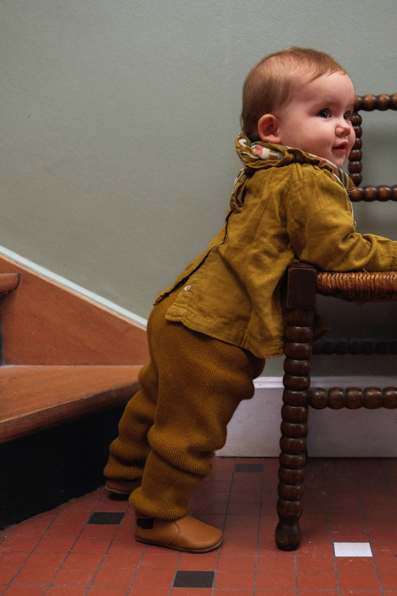 Bébé faisant ses premiers pas en hiver avec des chaussons en cuir souple marron