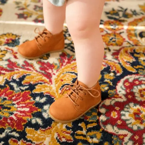 Enfant qui porte les chaussures lou caramel sur un tapis coloré