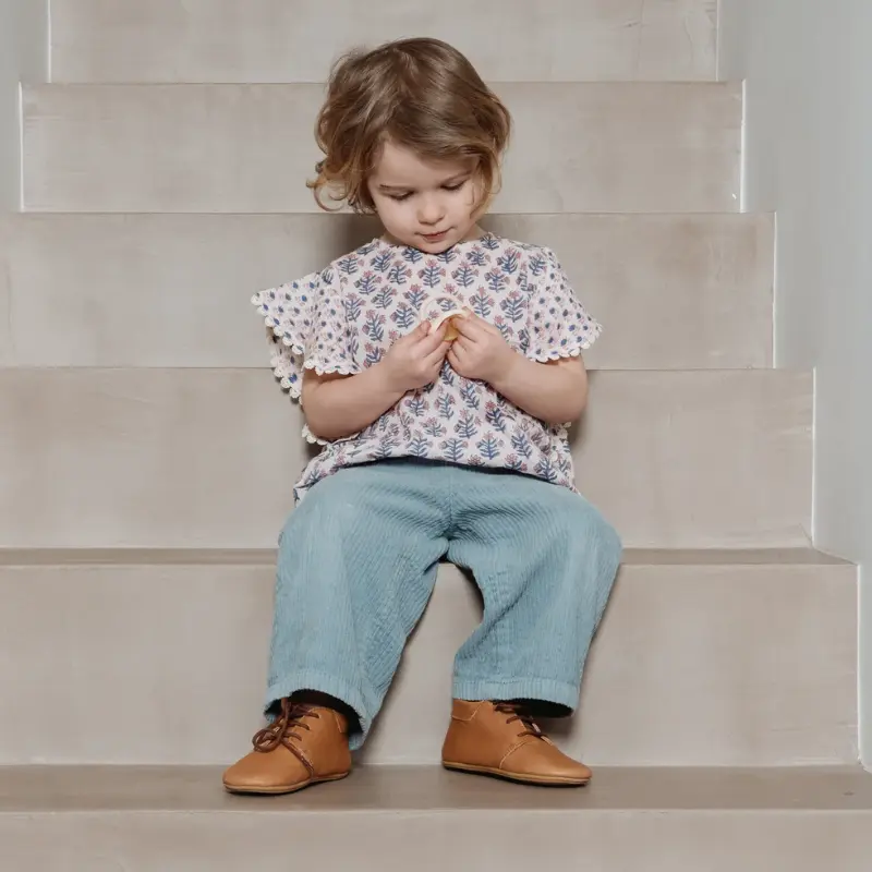 enfant portant les chaussons colombe marron assise sur des marches