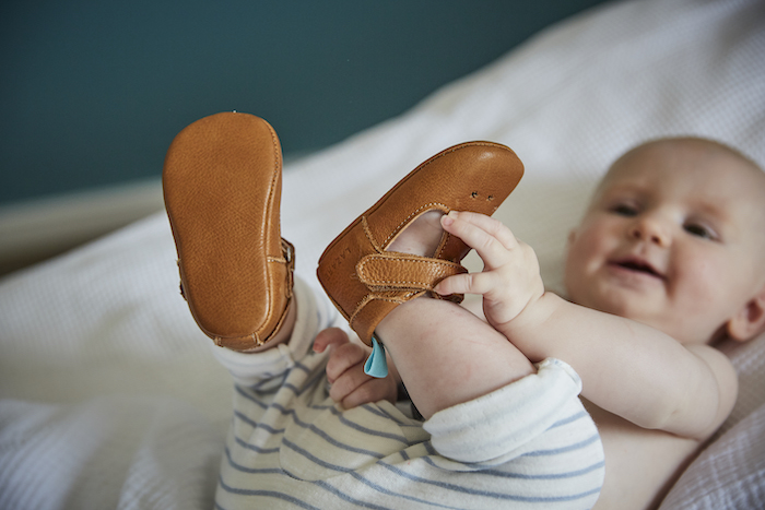 bébé portant des chaussons en cuir souple César marron attrapant ses pieds