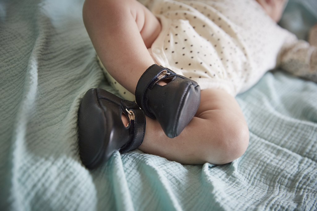 bebe allongé dans un lit avec un boy blanc et des chaussons en cuir souple bleu marine