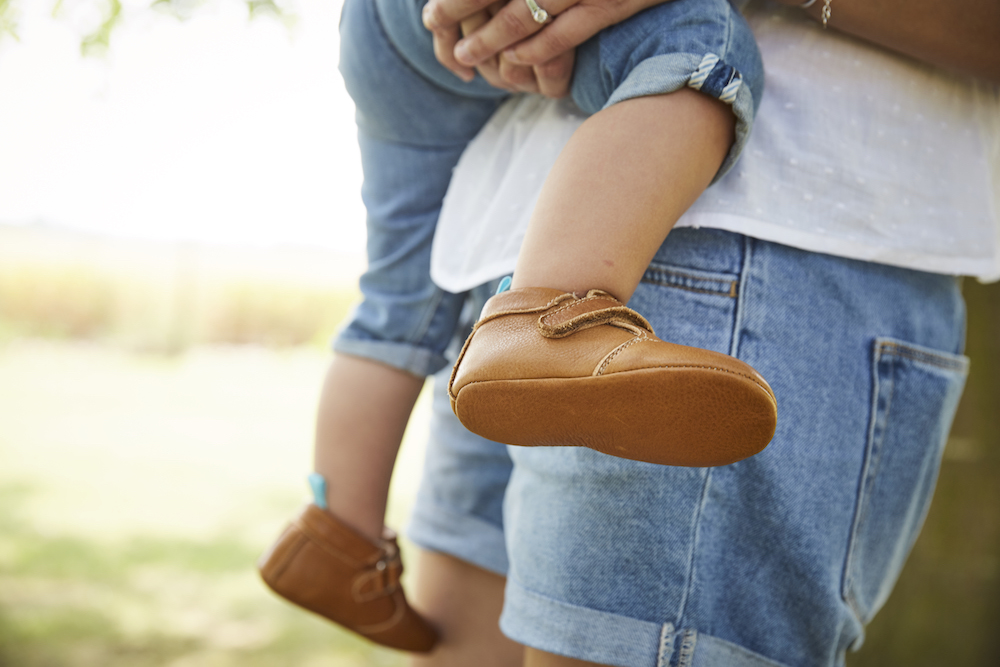 bebe avec des chaussons en cuir souple marron dans les bras d'un homme