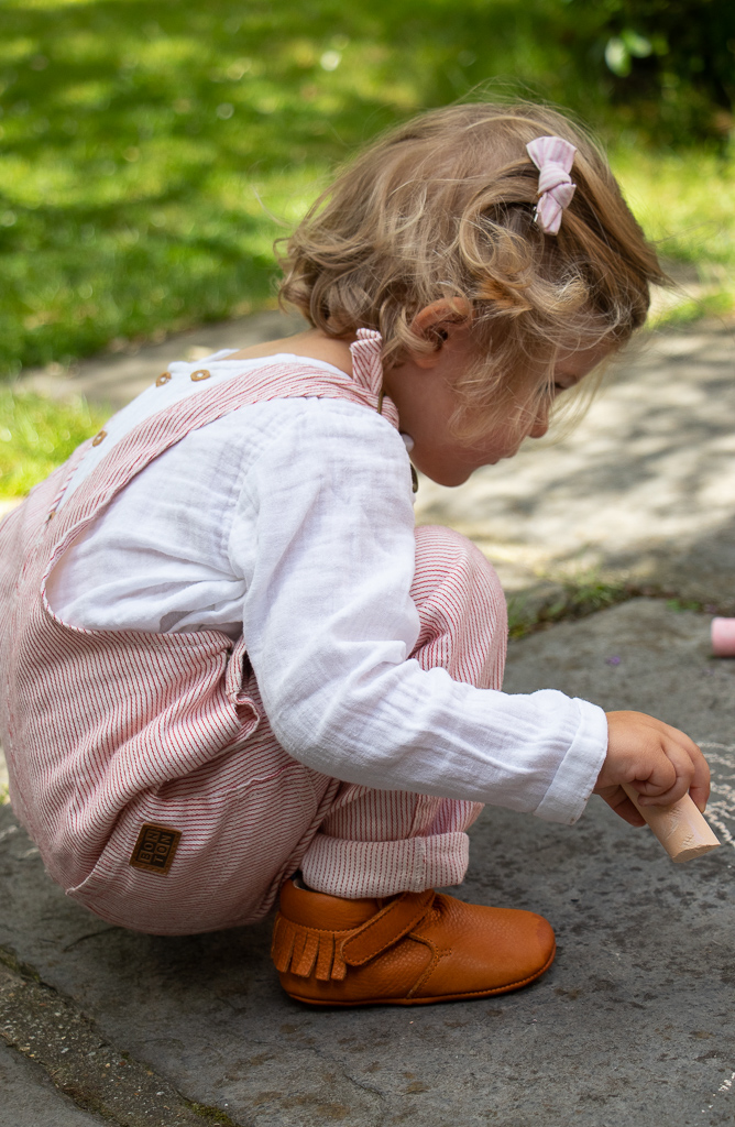 fille bebe entrain de jouer dehors, elle porte des chaussons en cuir souple premiers pas avec des semelles antidérapantes