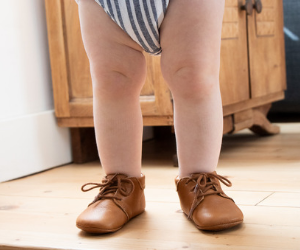 jambes de bébé debout avec des chaussons à lacets en cuir souple marron