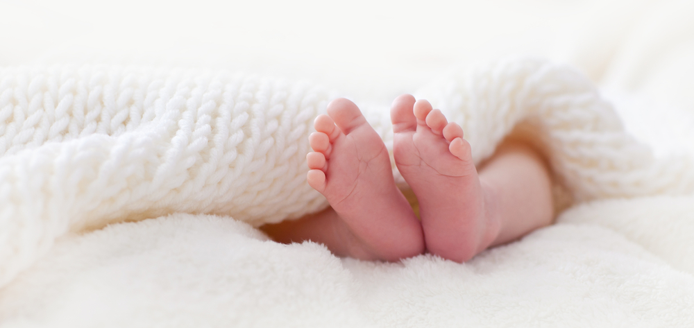 pieds d'un bébé sous une couette blanche