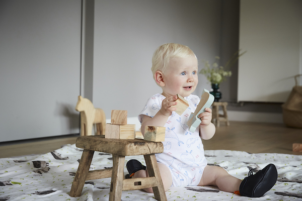 bébé en body assis par terre portant des chaussons en cuir souple bleu marine et jouant avec des jeux en bois