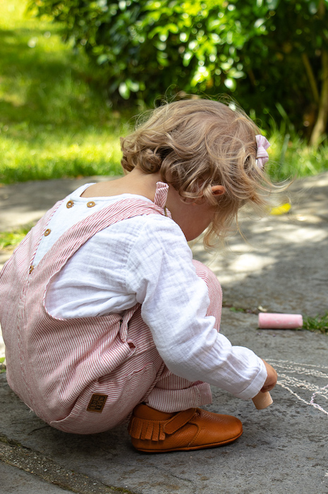 petite fille accroupie avec des chaussons en cuir souple marron à franges sur talon