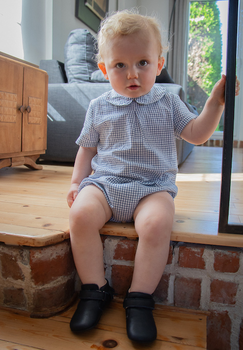 bébé assis sur une marche portant des chaussons en cuir souple bleu marine