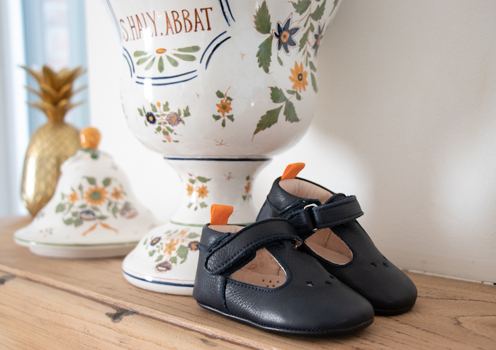 Chaussons bébé en cuirs souple César bleu marine posés sur une planche en vois devant un vase en verre