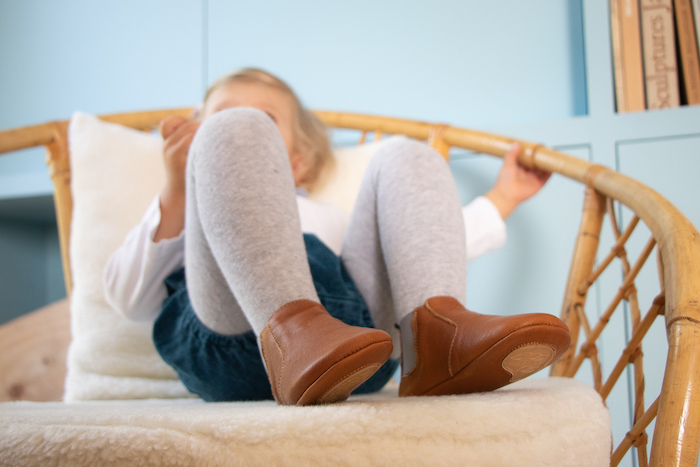 Petite fille assise dans un fauteuil portant des chaussons en cuir souple marron élastique gris