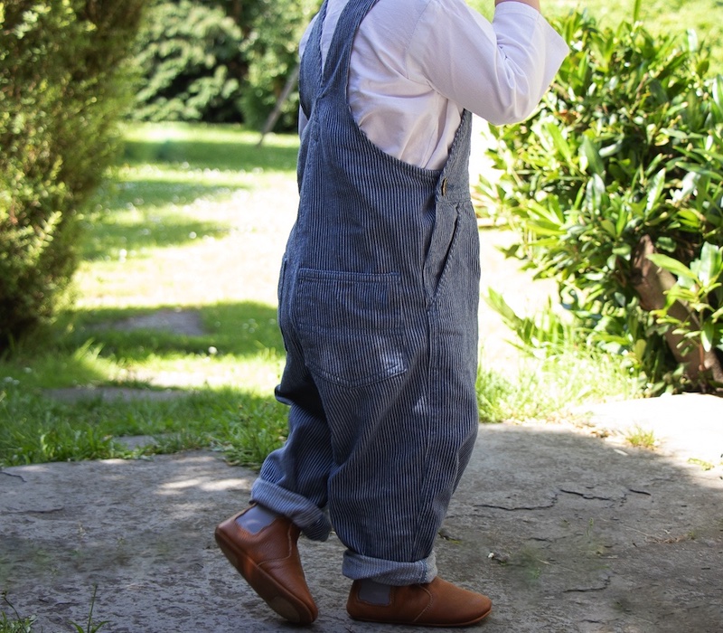 enfant debout en salopette dehors portant des chaussons en cuir Oscar marron élastique gris