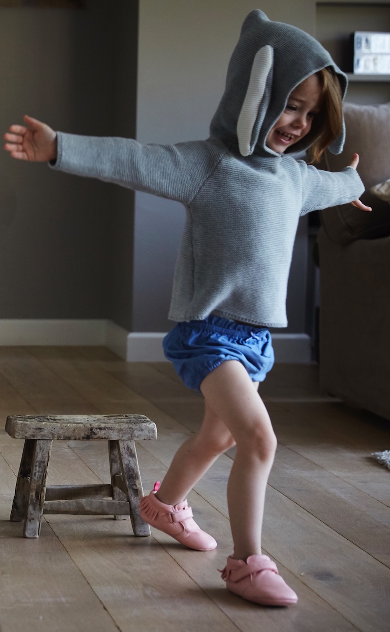 petite fille debout, bras ouverts portant des chaussons en cuir souple rose à franges