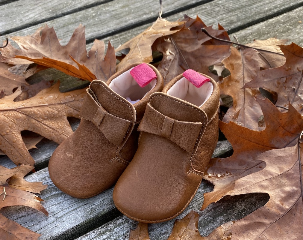chaussons bébé en cuir souple Arielle chocolat avec languette rose posés sur des feuilles d'automne
