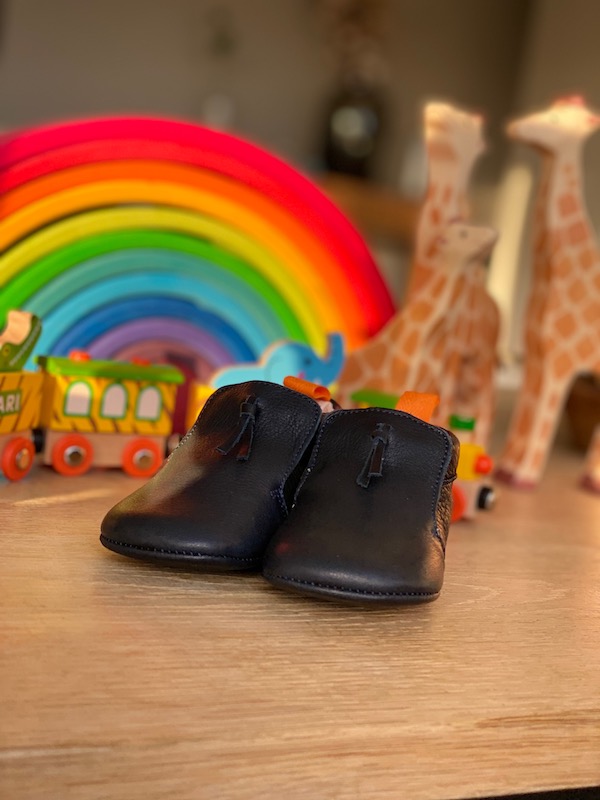 chaussons bébé en cuir souple Madeleine bleu marine posés sur une table devant un arc en ciel en bois