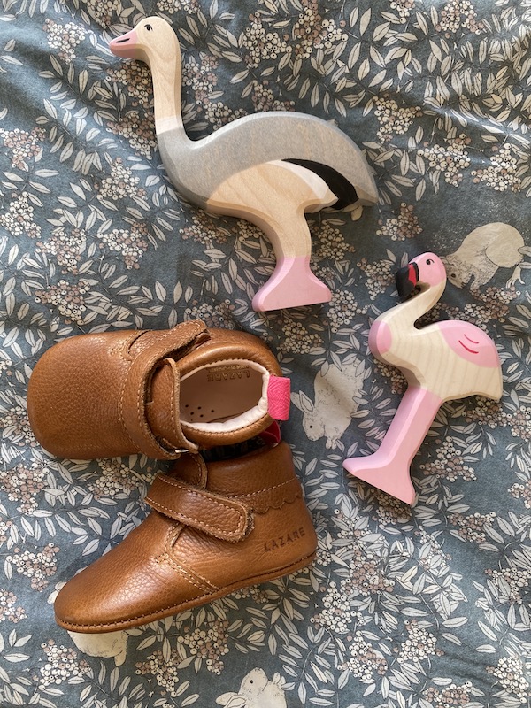 chaussons bébé Suzanne marron en cuir souple posés sur un drap avec des oiseaux en bois en décoration