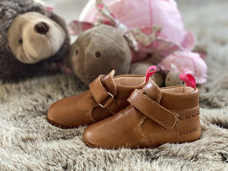 chaussons bébé en cuir souple Suzanne marron posés sur un plaid avec des peluches en fond