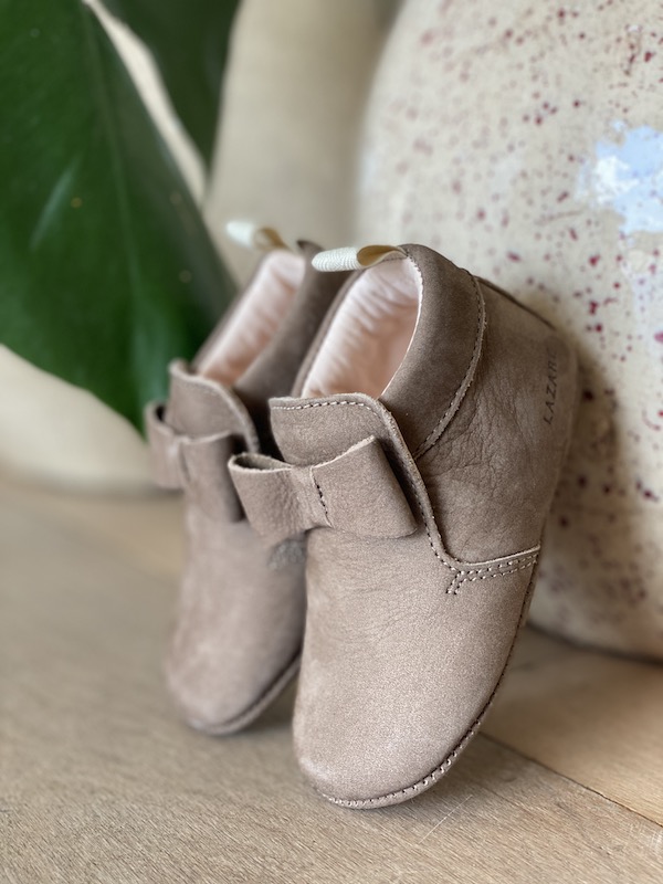 chaussons bébé Arielle en cuir nubuck taupe avec neuf sur le dessus posés devant un vase