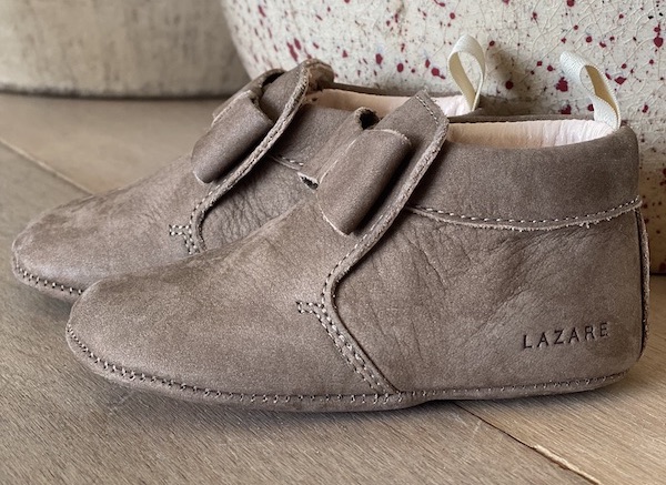 chaussons bébé Arielle en cuir nubuck taupe avec neuf sur le dessus posés devant un vase