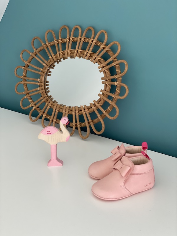 chaussons bébé Arielle en cuir souple rose avec noeud sur le dessus posés devant un miroir